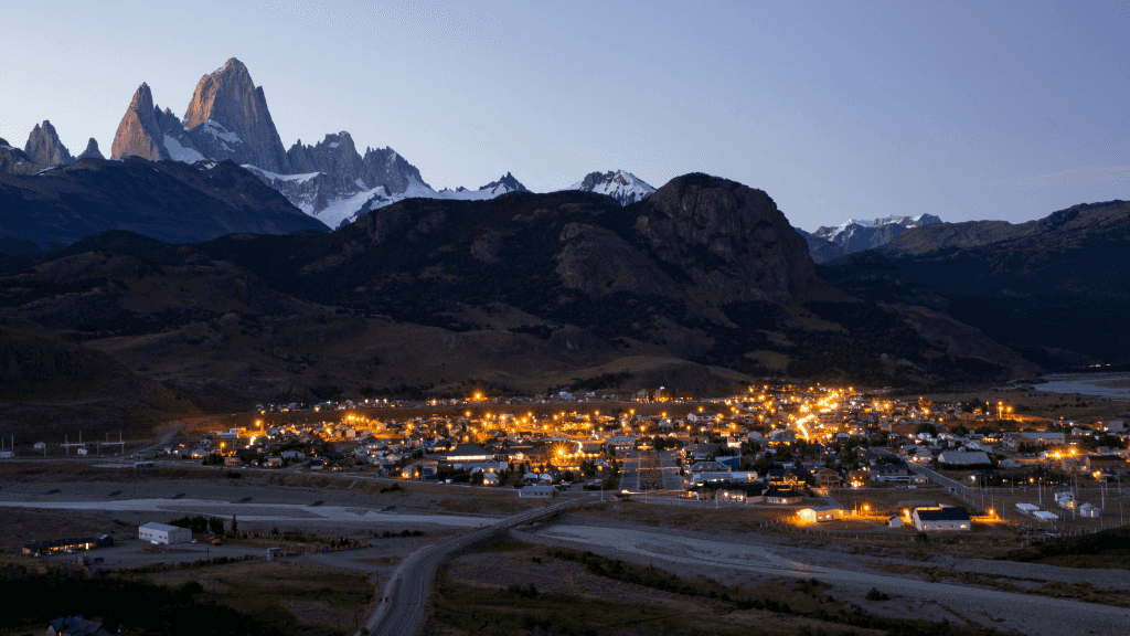 El Chaltén town illuminated at dusk beneath Fitz Roy mountain, visited during the 9-day Patagonia Hiking Tours - Blue Heart Adventure. Gateway to adventure.