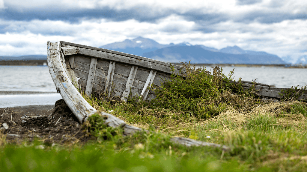 Old wooden boat on Patagonian shore with mountains in background, seen during the 9-day Blue Heart Adventure hiking tour. Rustic charm in remote landscapes.
