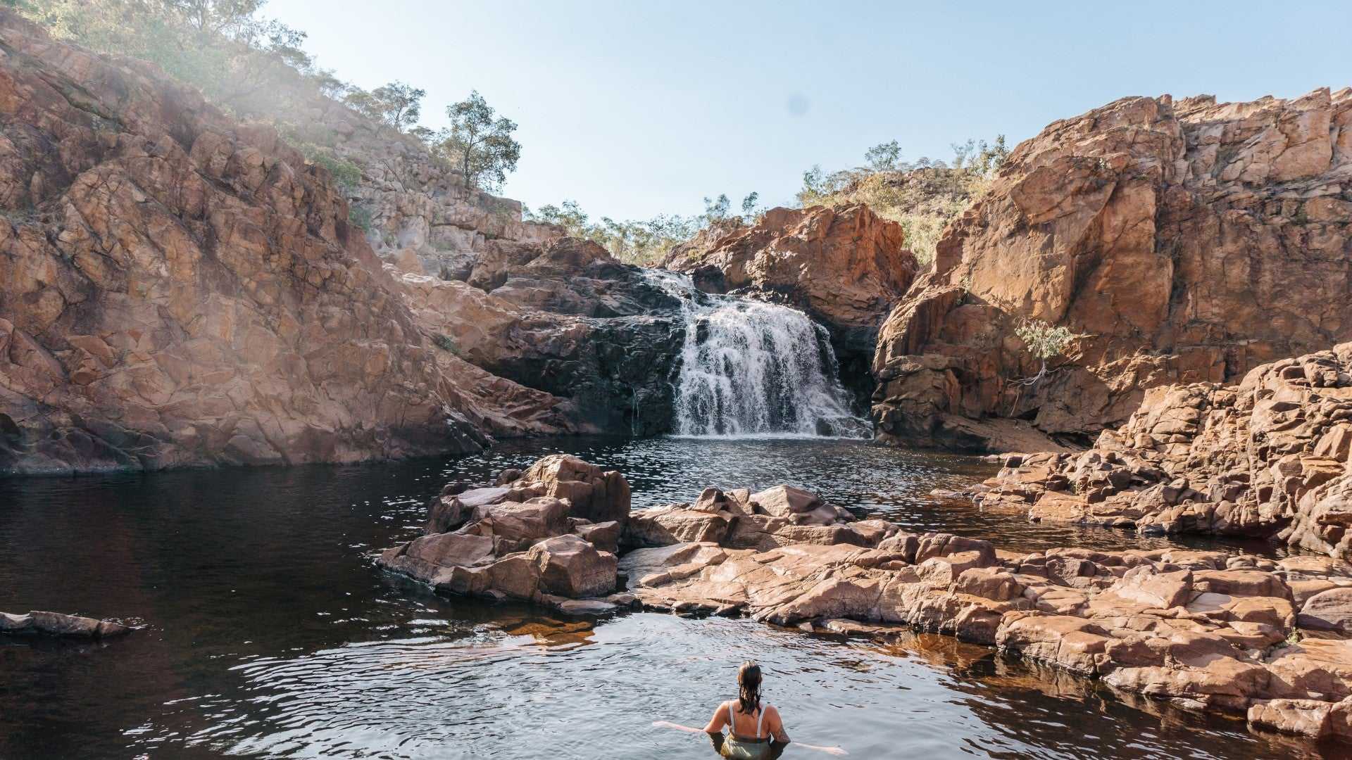Woman swims near waterfall in rocky gorge on Kakadu Katherine Gorge Tour | 4-Day Comfort Travel. Natural pool in remote wilderness.