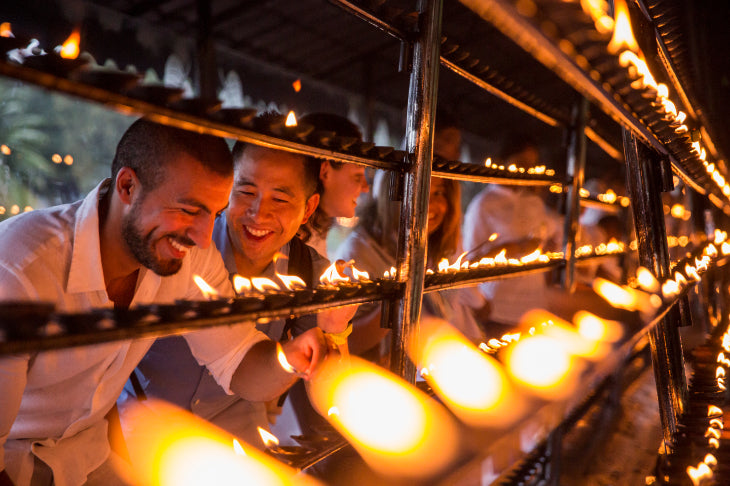 Travelers lighting oil lamps at Sri Lankan temple. Explore Sri Lanka - Land & Sea Tour Options includes spiritual and cultural rituals.
