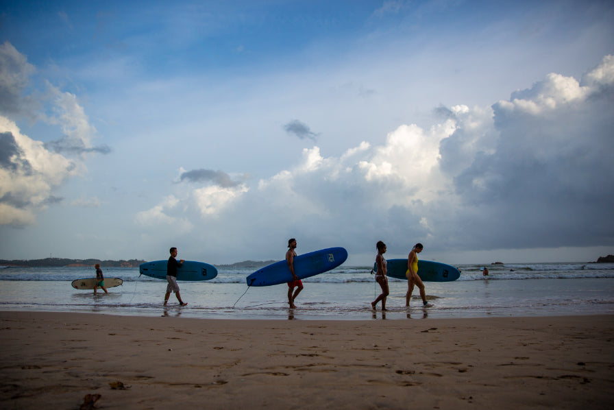 Group carrying surfboards along beach at dusk. Explore Sri Lanka - Land & Sea Tour Options includes surfing and coastal activities.