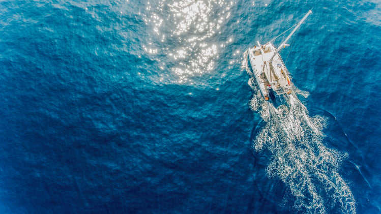 Aerial view of catamaran cruising through deep blue ocean. Explore Sri Lanka - Land & Sea Tour Options offers serene sailing experiences.