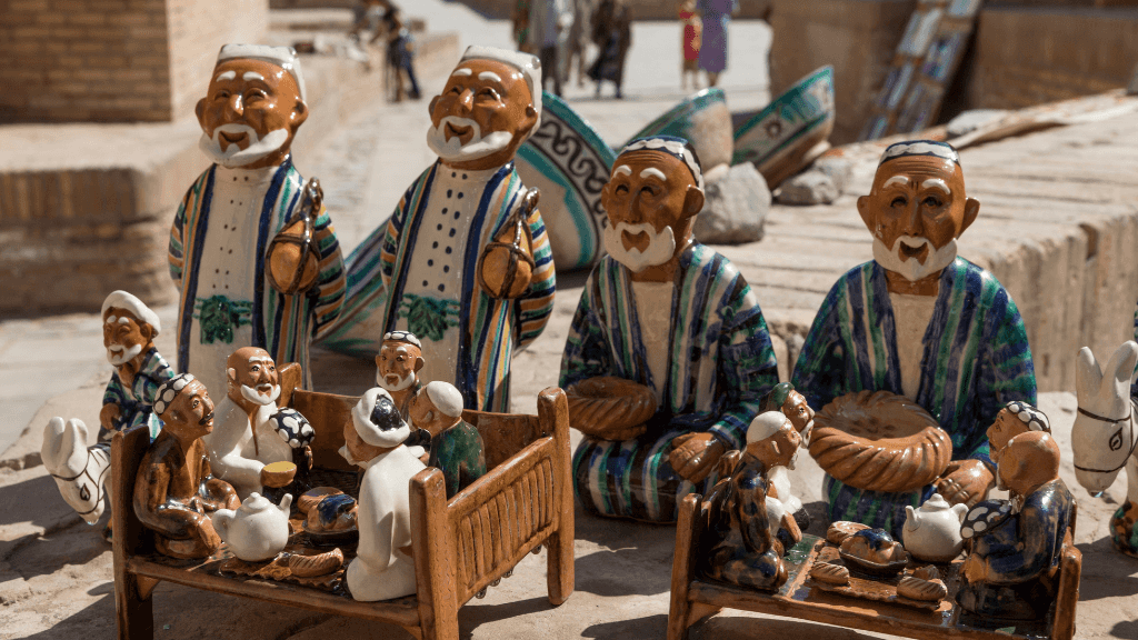 Handcrafted ceramic figurines of Uzbek elders at a market, a cultural souvenir on the Silk Road Cities Tour - Central Asia Adventure.