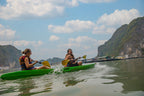 Two women kayaking in calm waters surrounded by limestone cliffs. Outdoor water activity on Vietnam Hiking and Cycling Tour.