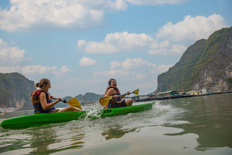 Two women kayaking in calm waters surrounded by limestone cliffs. Outdoor water activity on Vietnam Hiking and Cycling Tour.