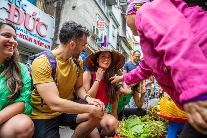 Traveler laughing with local vendor at a Vietnamese street market. Cultural interaction on Vietnam Hiking and Cycling Tour.
