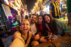 Group selfie at a lively night market in Vietnam. Social nightlife experience on Vietnam Hiking and Cycling Tour.