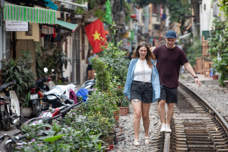 Couple walking along train tracks in Hanoi’s café-lined street. Romantic stroll on Vietnam Hiking and Cycling Tour.