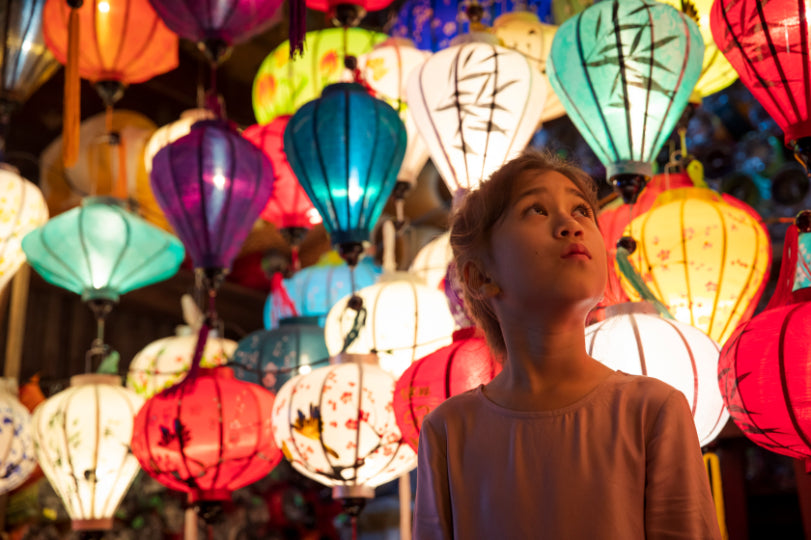 Child admiring colorful lanterns in a Vietnamese night market. Cultural charm on Vietnam Hiking and Cycling Tour.