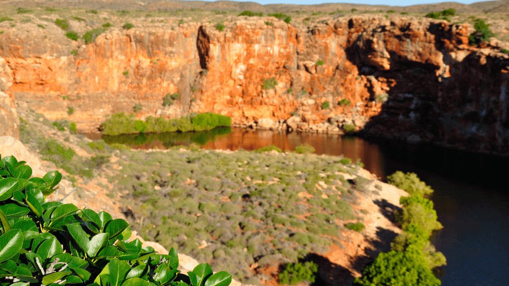 Scenic view of rugged cliffs and greenery near a tranquil waterhole in Cape Range National Park, perfect for adventure tours.