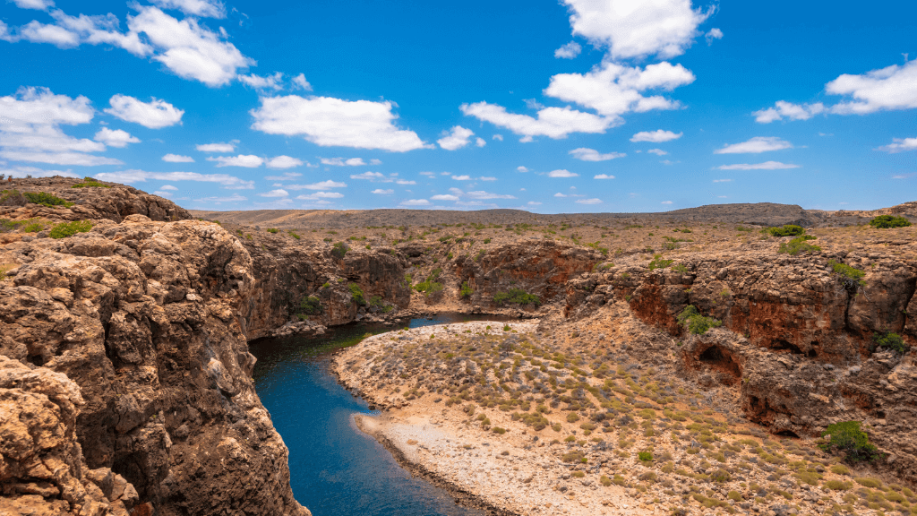 Rugged landscape of Cape Range National Park with limestone canyons and a winding river under a bright blue sky.