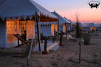 Tented camp setup on a sandy area with sunset or sunrise sky.