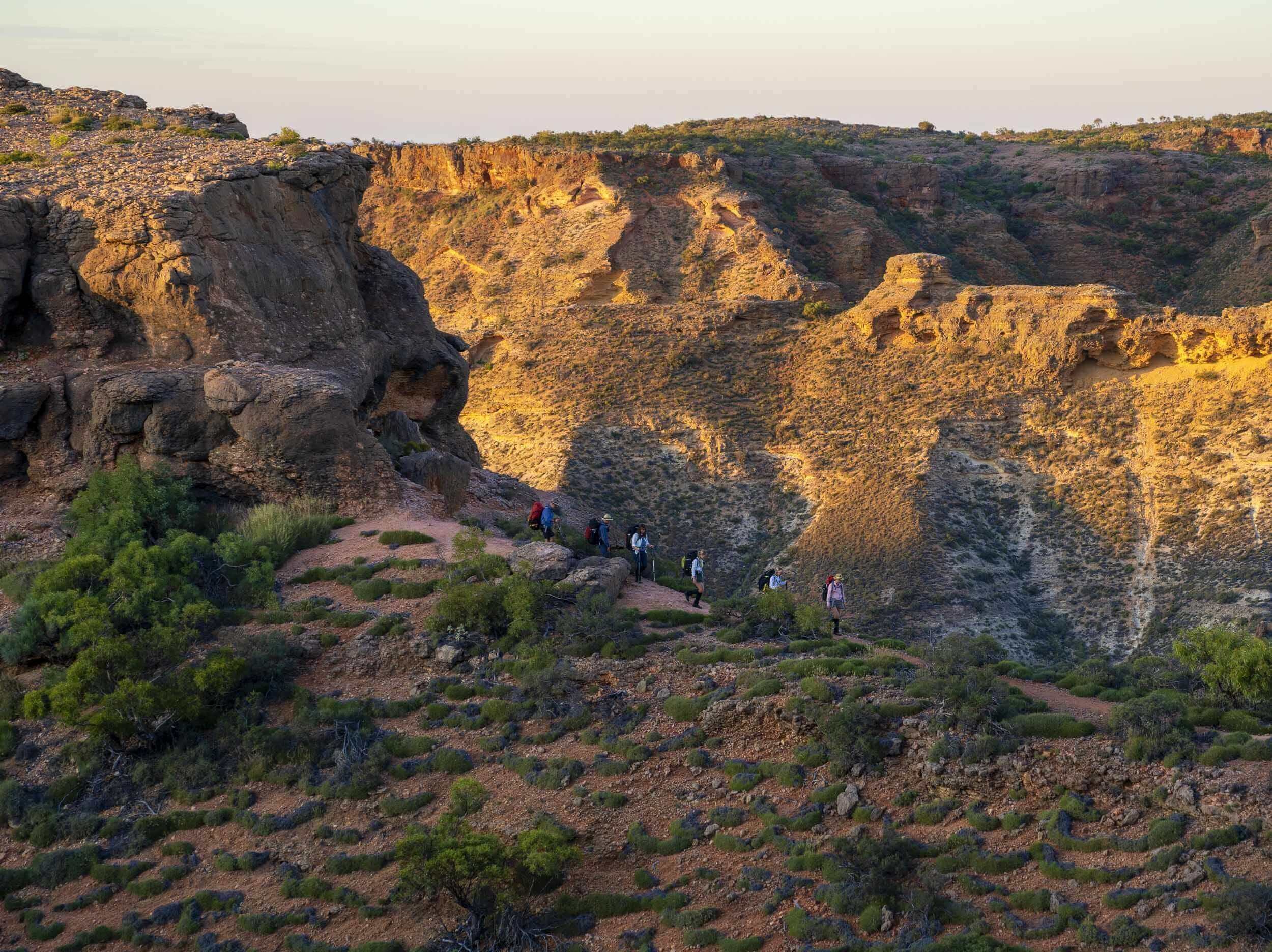 Group trekking along rugged cliffs in Cape Range National Park, showcasing stunning Australian wilderness.