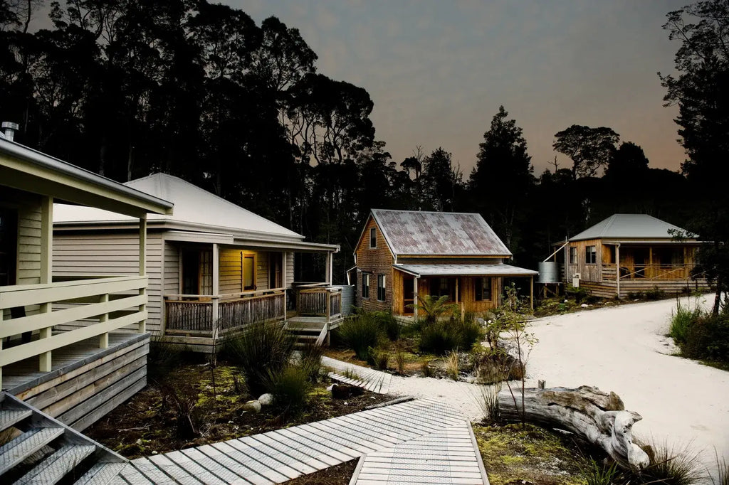 Three wooden cabins with a pathway leading to them, surrounded by trees.