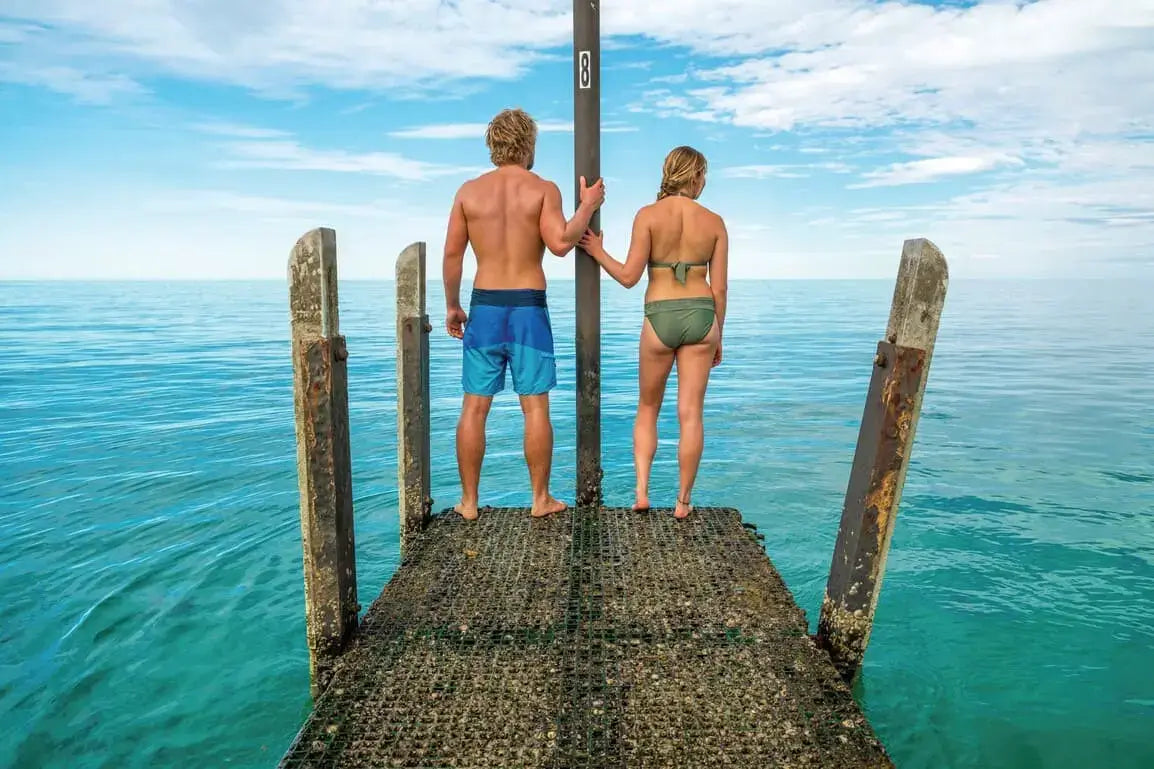 Couple standing on jetty overlooking turquoise waters at Shark Bay on West Coast Road Trip. Romantic coastal stop in Western Australia.