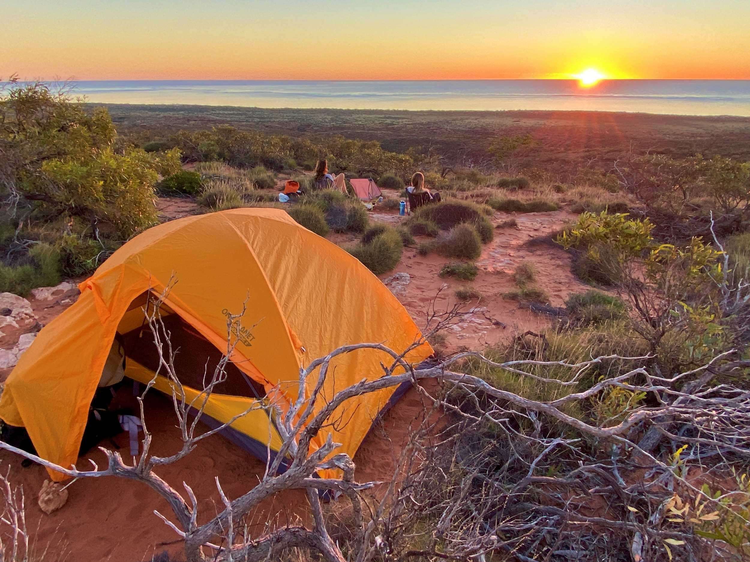 Sunset view over the Ningaloo Coast with an orange tent set in rugged terrain, perfect for adventure tours.