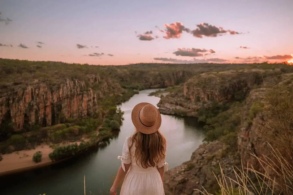 A traveler in a straw hat admires the stunning landscape of a river canyon at sunset in Australia.